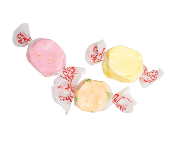 Three pieces of Sweet Heat Salt Water Taffy – Freeze-Dried Candy with a Fruity Kick of Fire, in pink, yellow, and orange, are wrapped in white wax paper with red print and arranged on a white background.